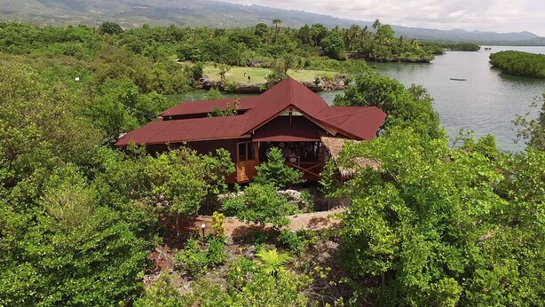 A lodge with a red roof nestled in a lush, green landscape with a river and mountains in the background. - Eskapo Verde Lodge Moalboal (Badian)