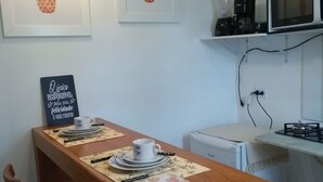 A dining area with a wooden table, chairs, a coffee machine, a microwave, and framed pineapple artwork on the wall.