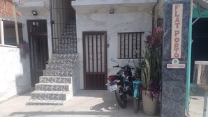 A building with a sign reading "FLAT PORTER" and a contact number. There are steps leading to a door with a barred window, a parked motorcycle, and potted plants.