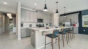 A modern kitchen with white cabinets, a central island with bar stools, and pendant lighting.