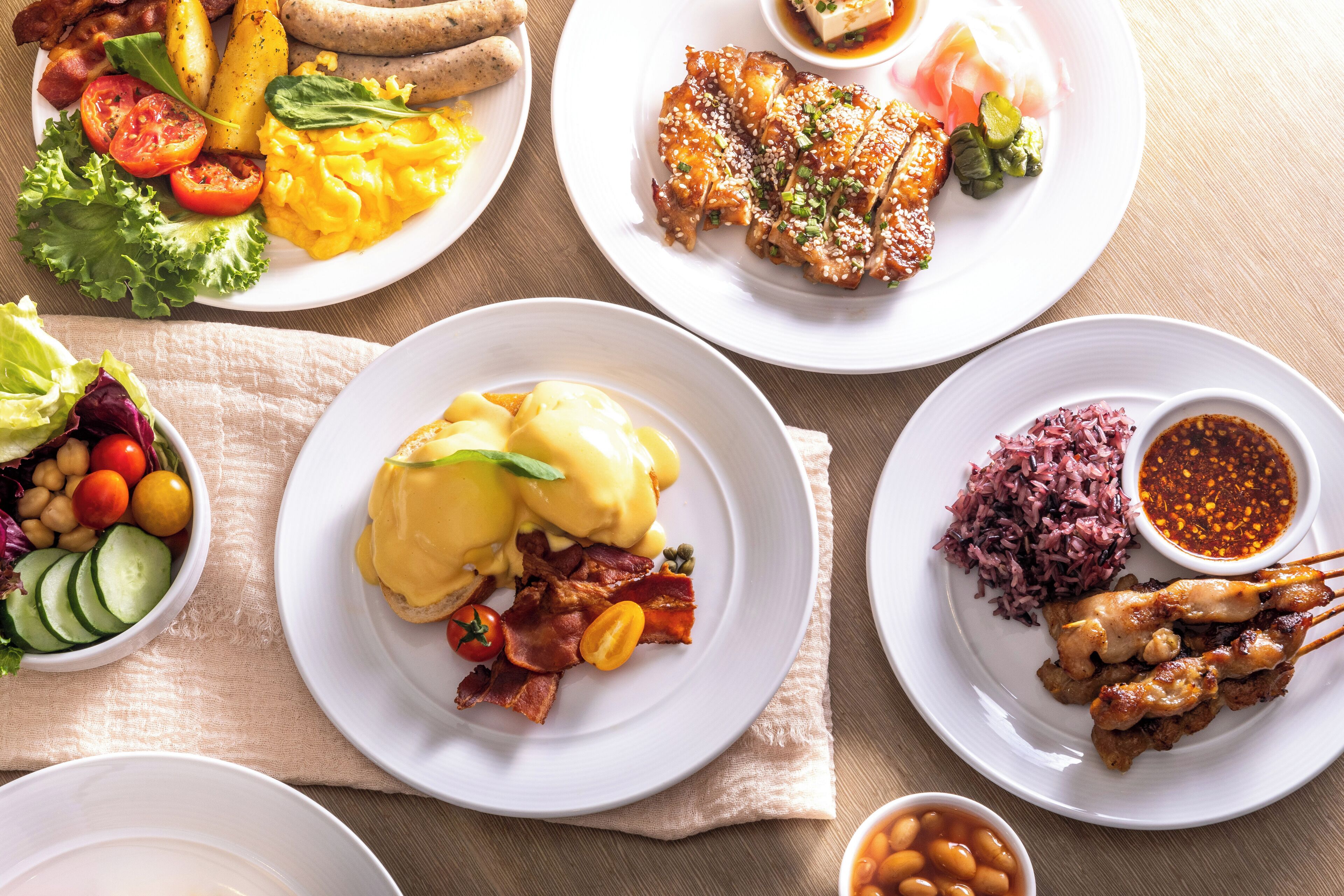 A variety of breakfast dishes including eggs, bacon, and sausages on white plates.
