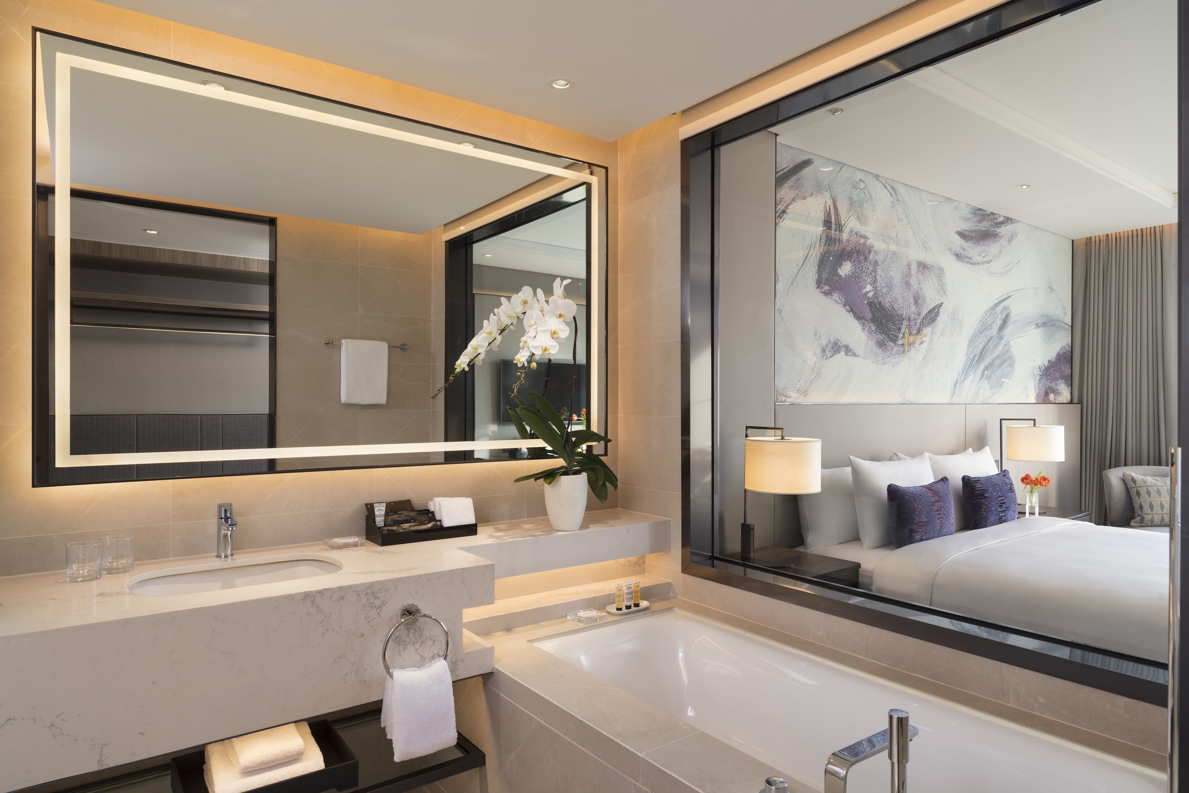 Un baño moderno con un espejo grande, un lavamanos, una bañera y una orquídea en maceta.