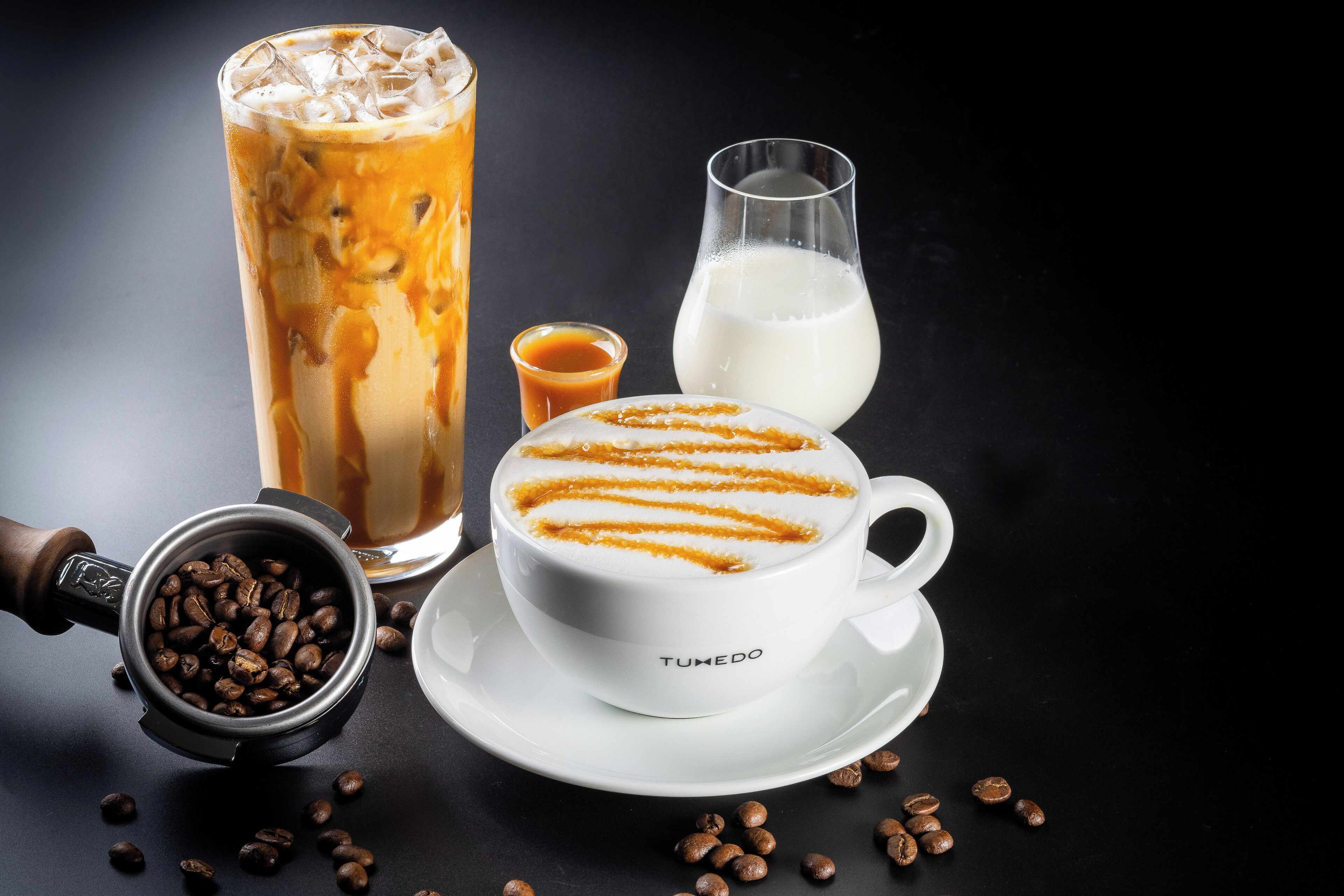 A cup of coffee with a latte art design, a glass of milk, and a tall iced coffee with ice cubes.