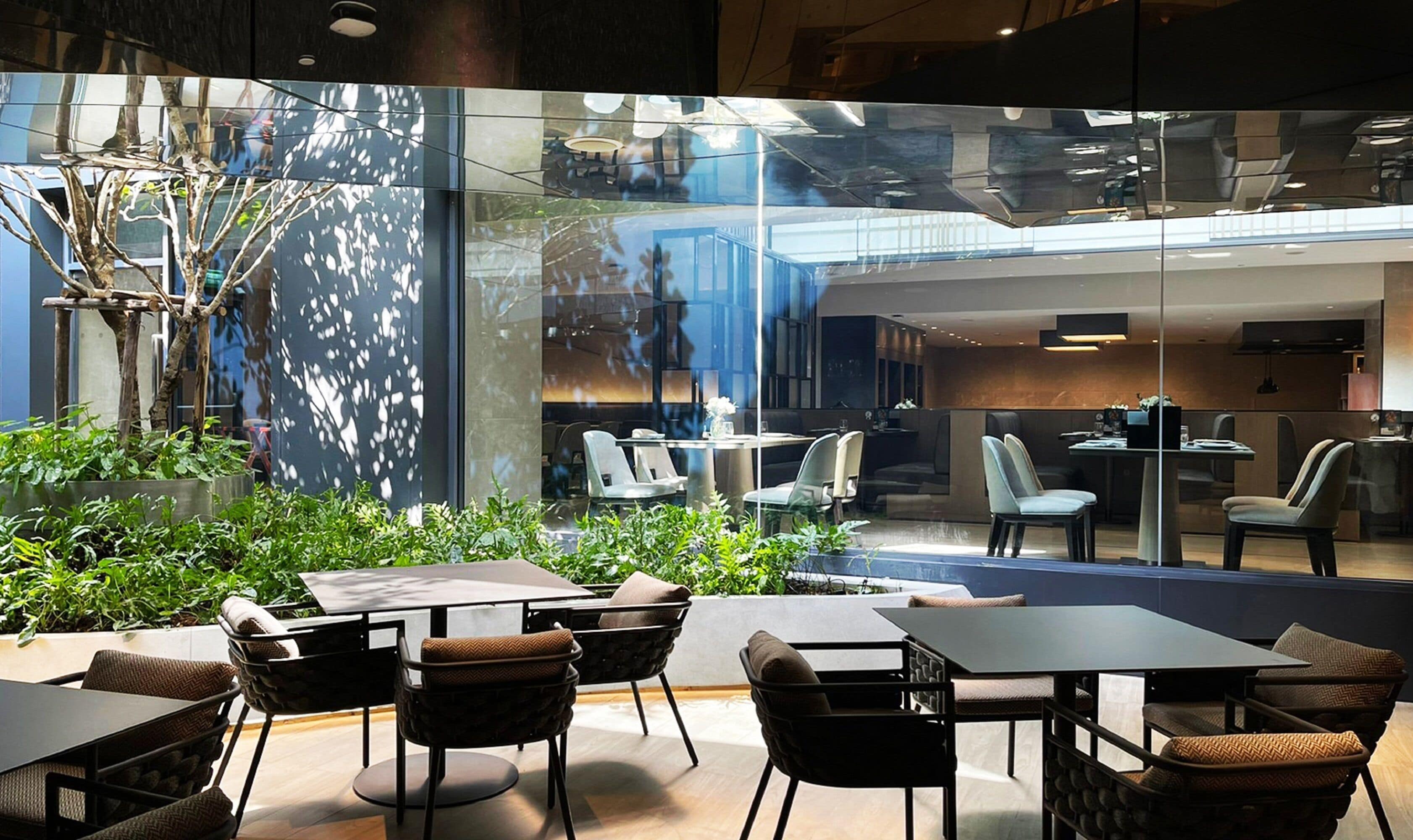 A modern indoor dining area with glass partitions, comfortable seating, and a view of the interior space.