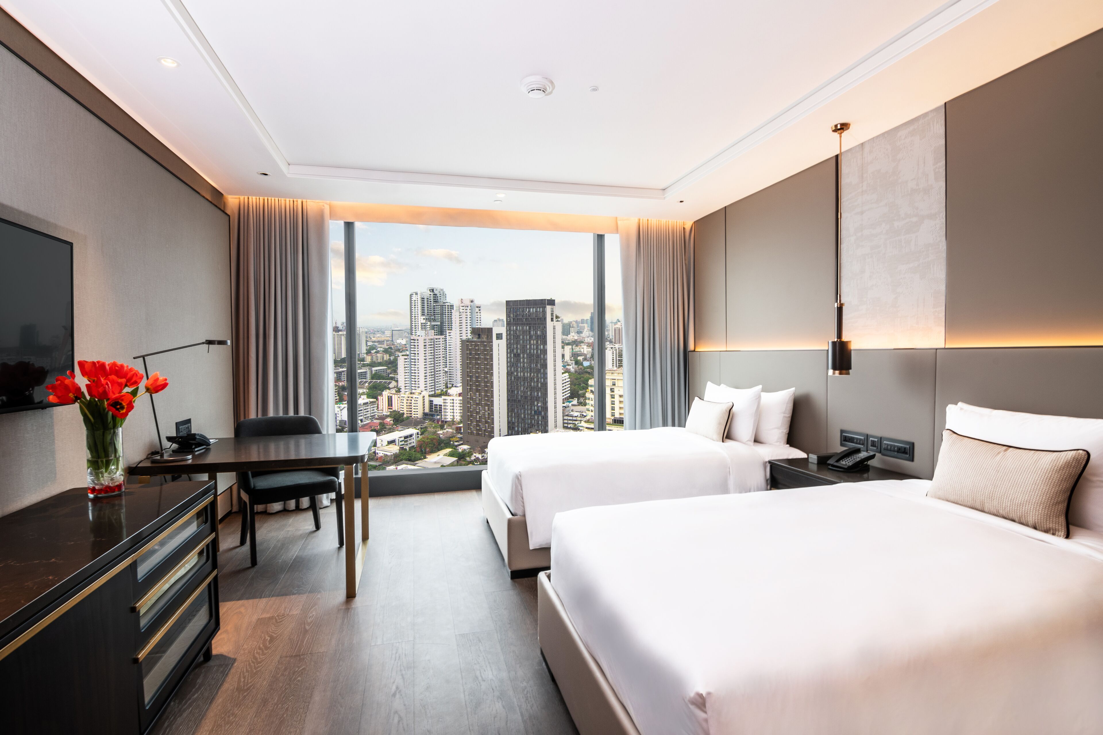 Habitación de hotel con dos camas, un escritorio, una silla, un televisor y un ventanal con vistas a la ciudad.