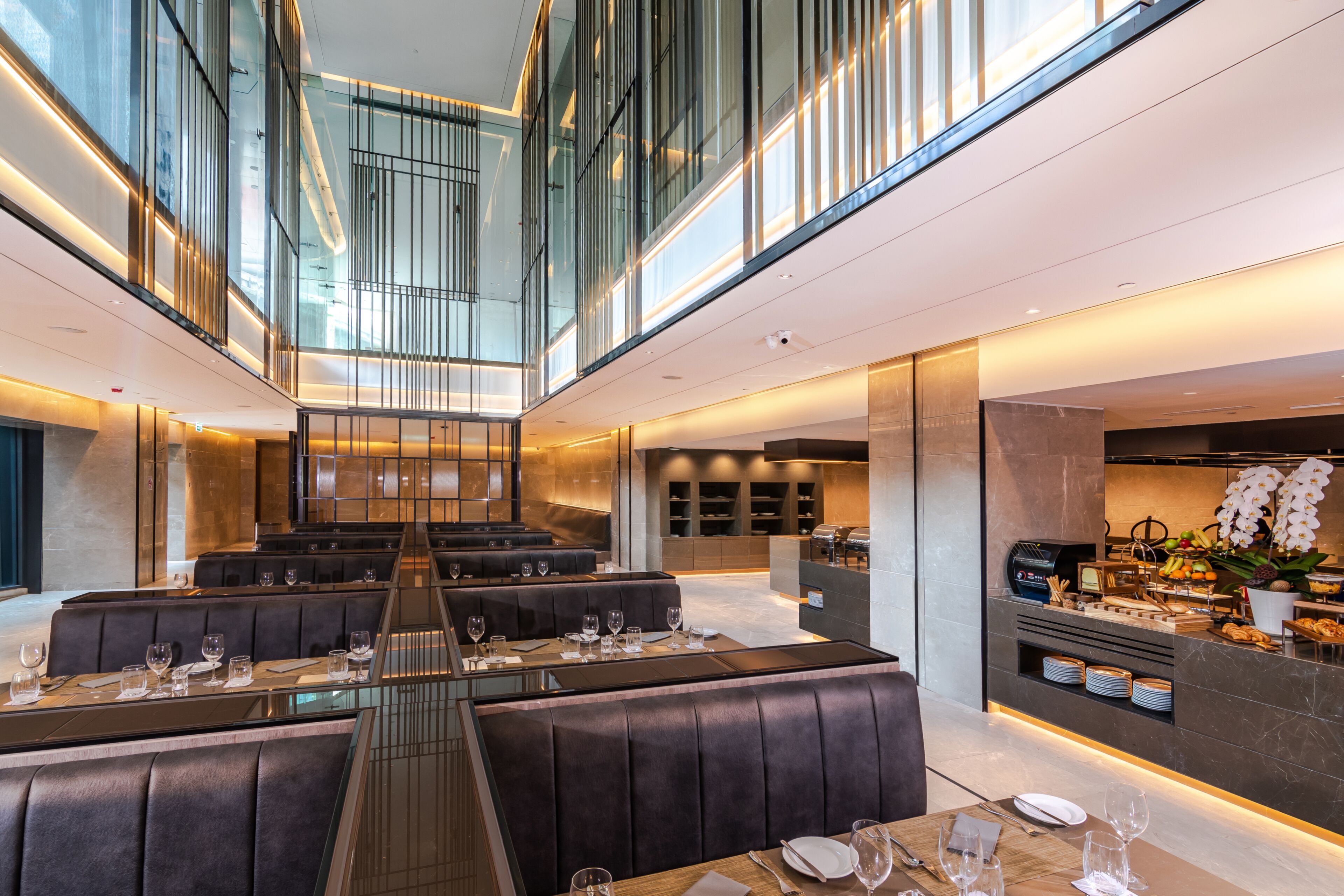 A modern restaurant with high ceilings, glass railings, and a central dining area with booths and tables.