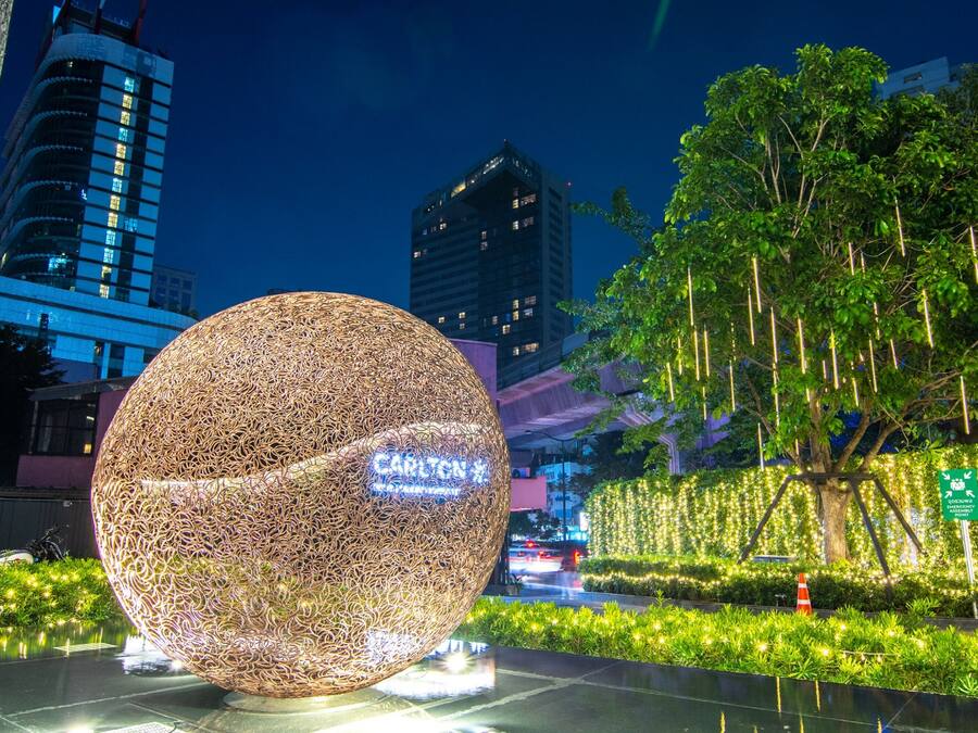 A spherical sculpture in an urban setting with buildings and greenery in the background.