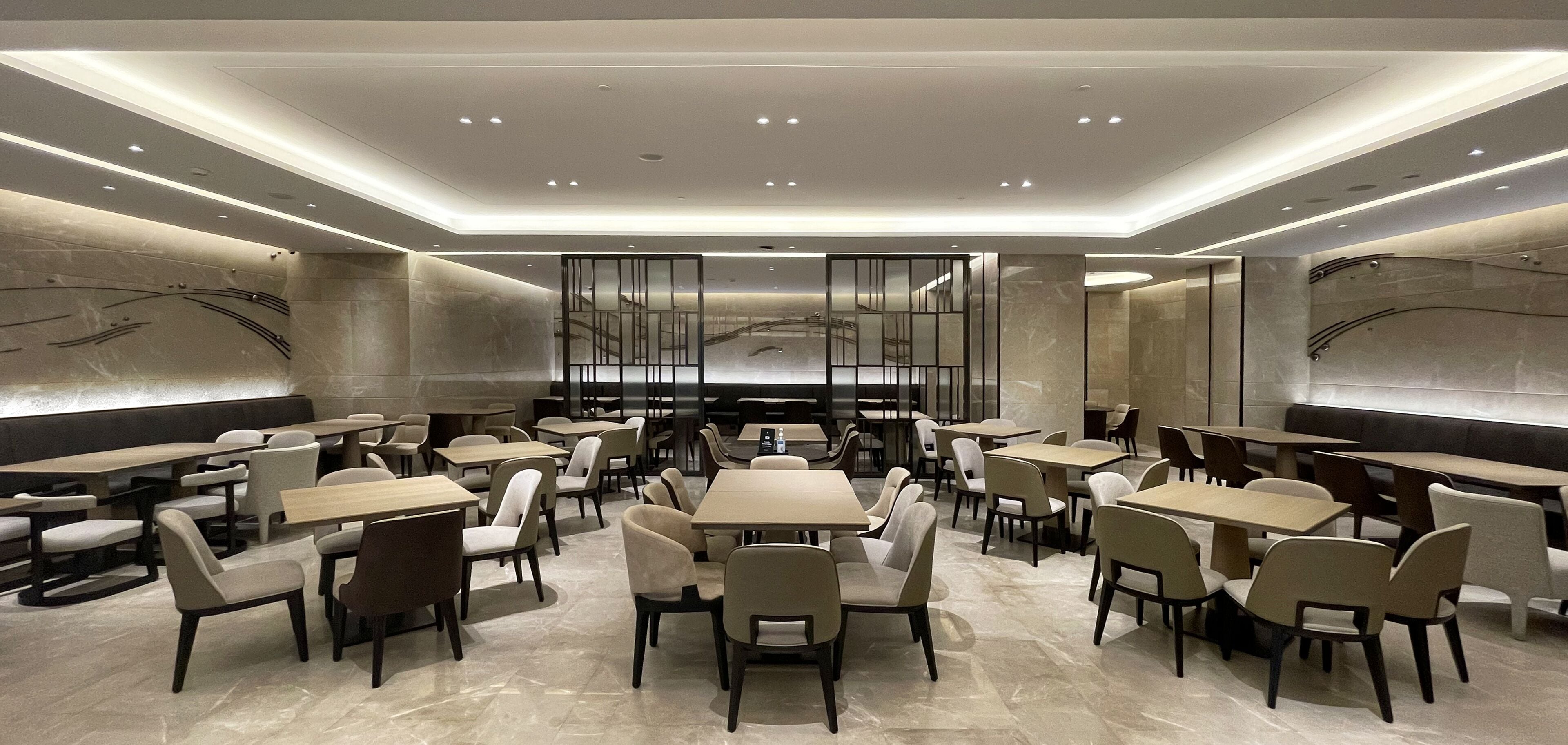 A modern restaurant with multiple dining tables and chairs, a central decorative wall, and recessed lighting.