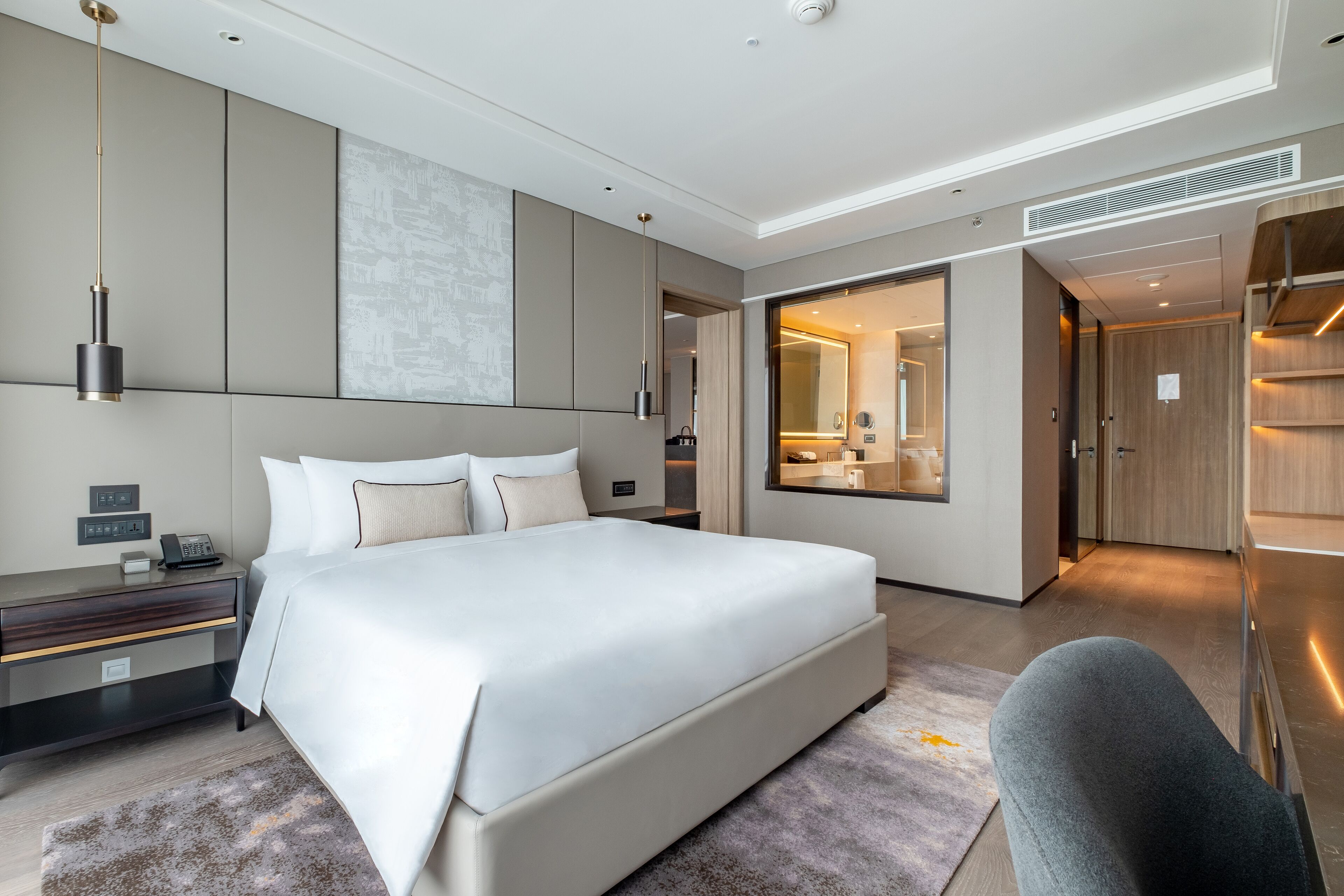 A modern hotel room with a large bed, a bedside table, a desk, and a walk-in closet.