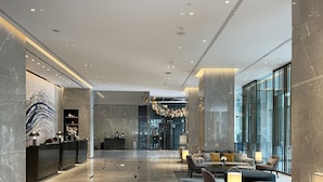 A modern lobby with marble floors, a reception desk, seating area, and large windows.