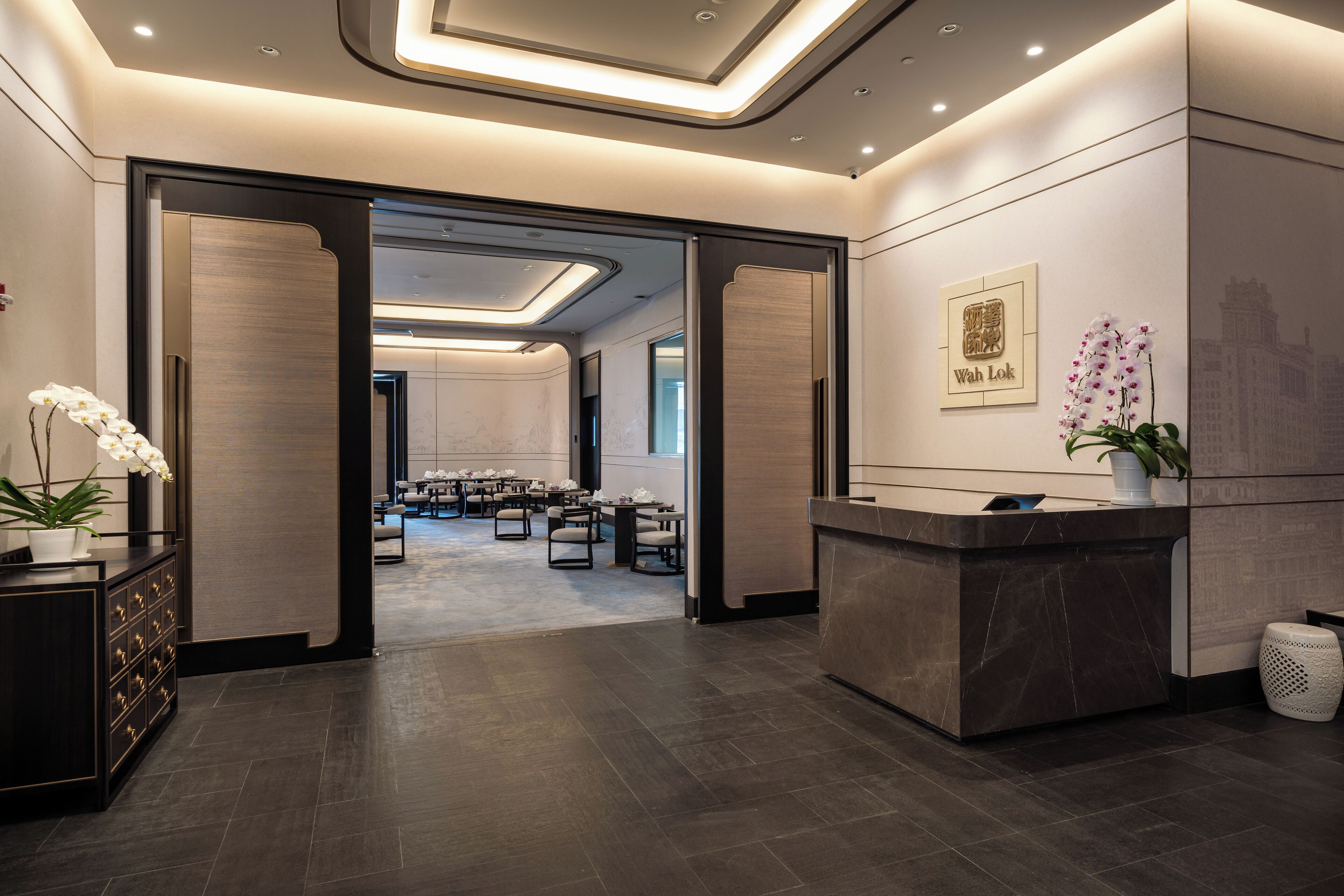 A hotel reception area with a modern design, featuring a reception desk, seating area, and a view into a conference room.