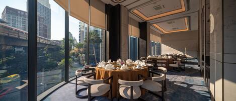 A modern dining area with round tables set for a meal, large windows offering a city view, and a spacious layout.