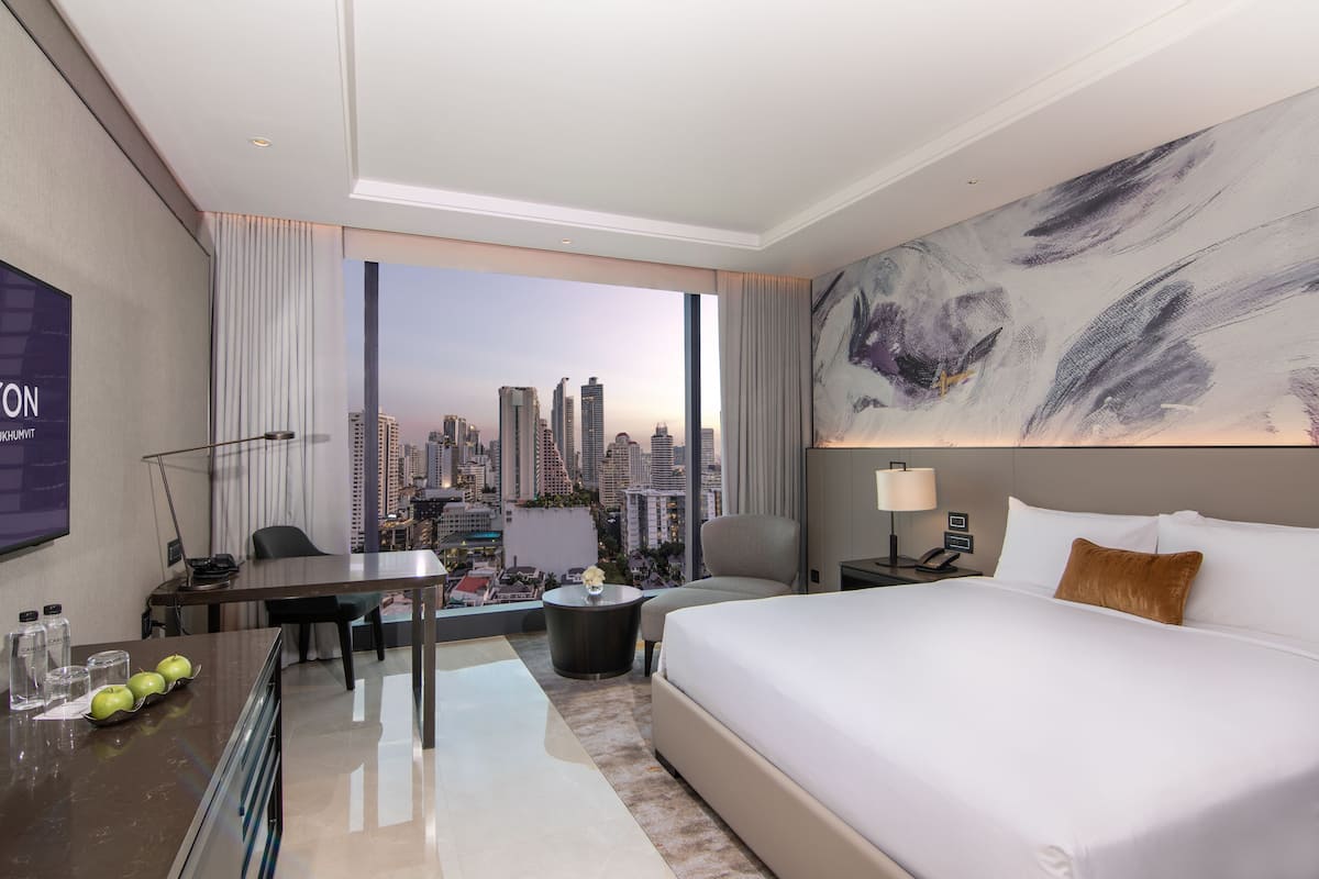 A modern hotel room with a large bed, a desk, and a view of the city skyline.