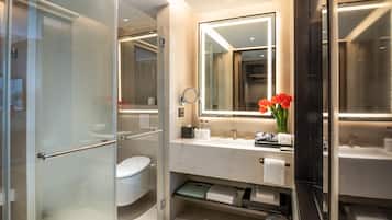 A modern bathroom with a glass shower enclosure, a toilet, a vanity with a mirror, and a vase with flowers.