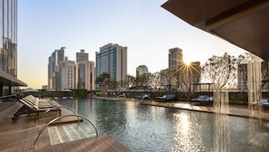 A rooftop pool with lounge chairs, a wooden deck, and a city skyline in the background.