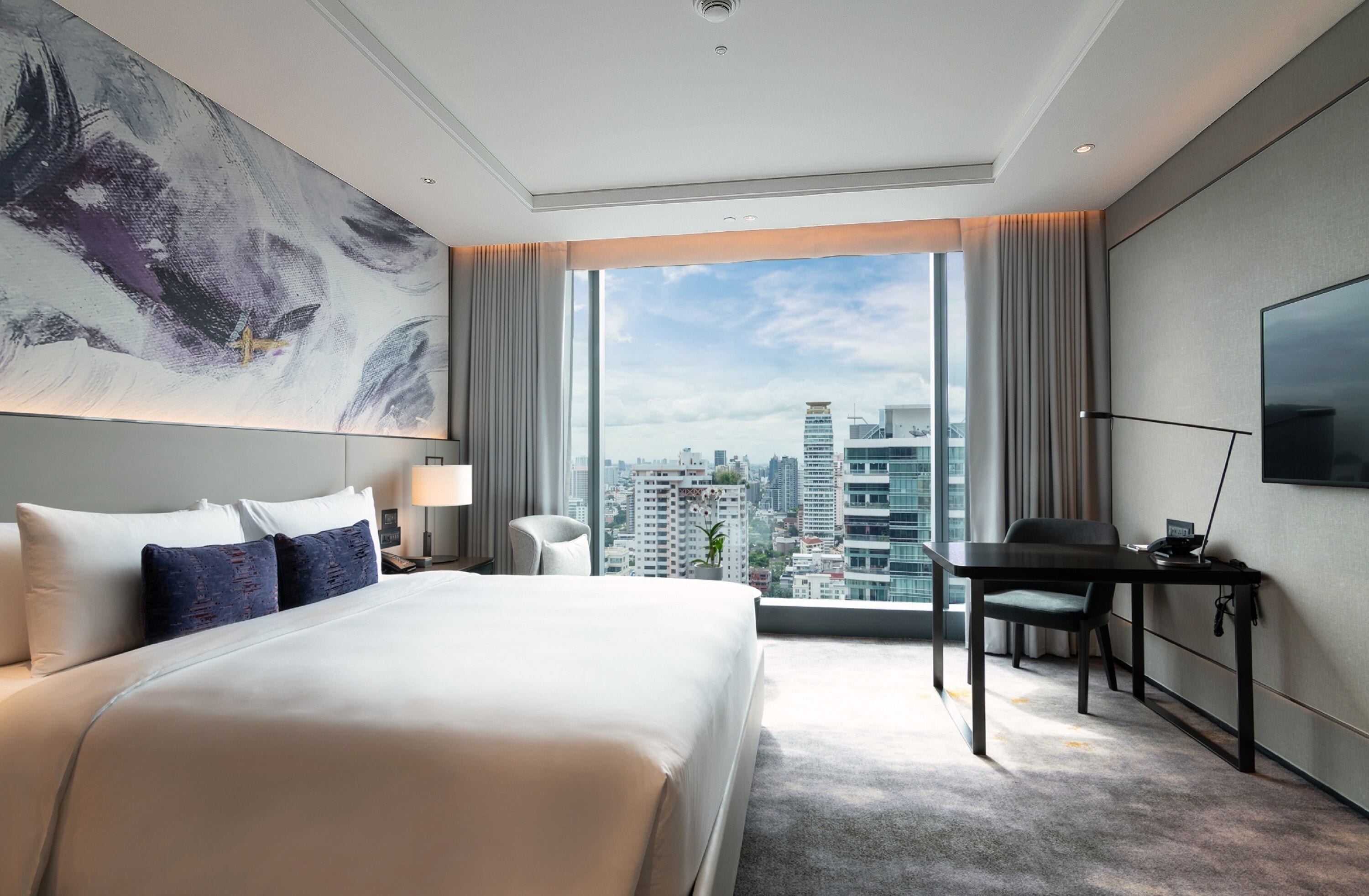 Una habitación de hotel moderna con una cama grande, un escritorio, una silla, un televisor y vistas a la ciudad.