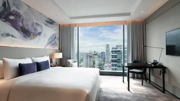 Una habitación de hotel moderna con una cama grande, un escritorio, una silla, un televisor y vistas a la ciudad.
