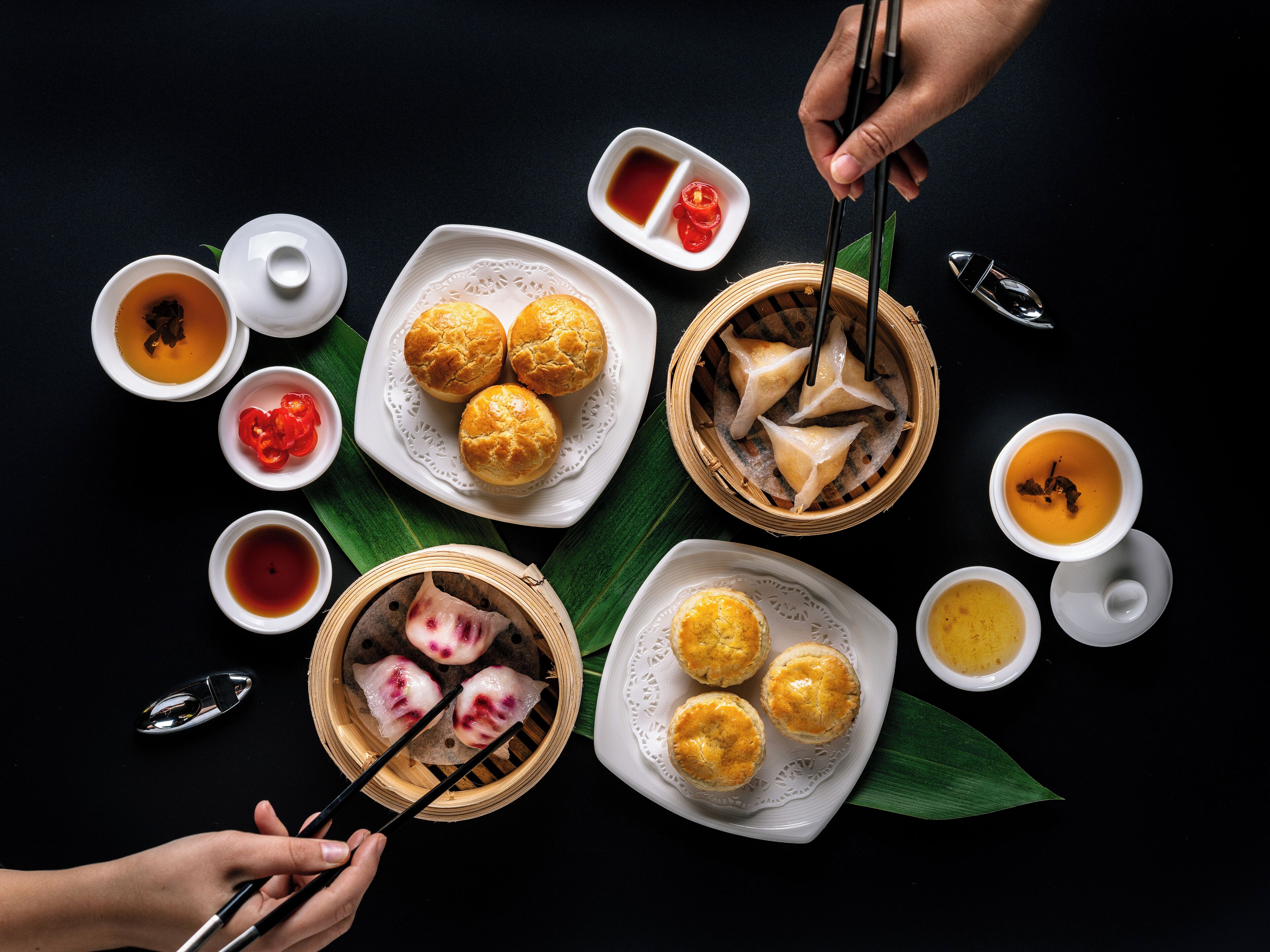 Diversos platos de comida asiática, como dumplings, bollos y sopa, sobre una mesa negra, junto a palillos.