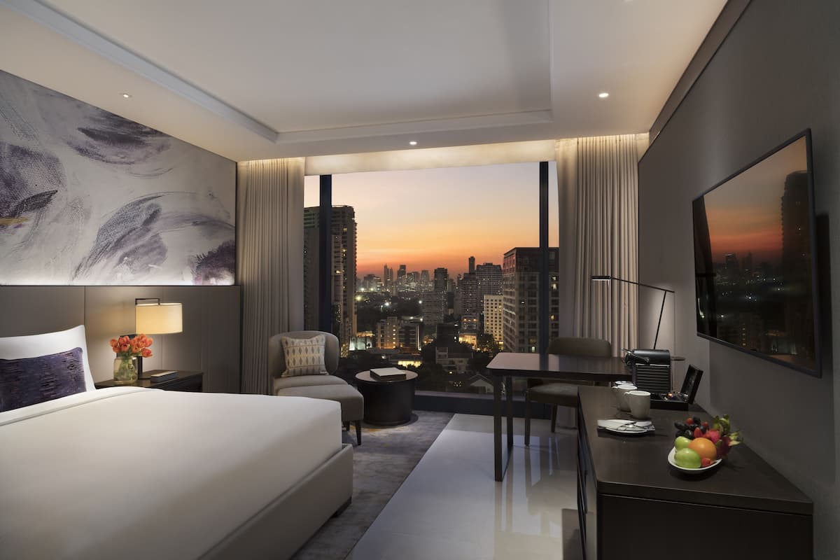 A modern hotel room with a city view, a bed, a desk, and a dining area.