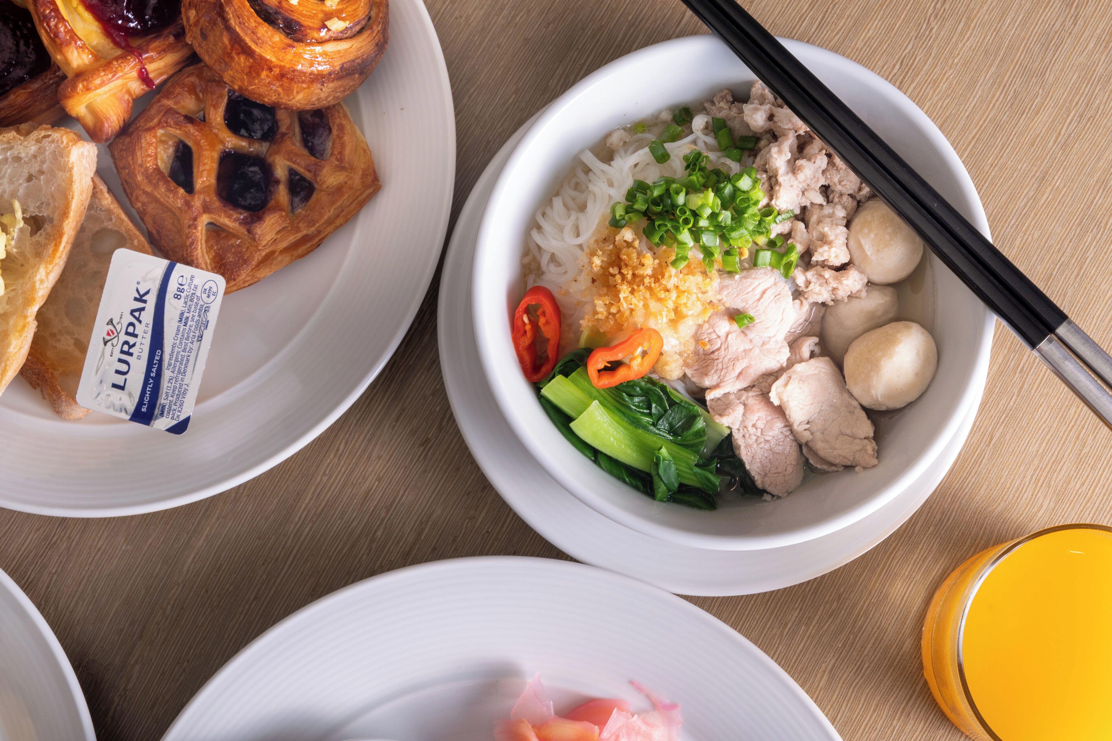 A table with various dishes including a bowl of rice with meat and vegetables, a plate of pastries, and a glass of orange juice.