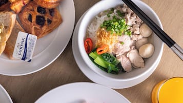 A table with various dishes including a bowl of rice with meat and vegetables, a plate of pastries, and a glass of orange juice.