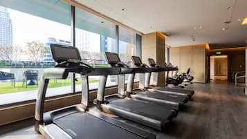 Una hilera de cintas de correr con pantallas digitales, suelo de madera y grandes ventanales con vistas a un paisaje urbano.