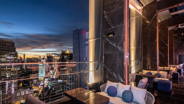 A high-rise hotel room with a city view, modern furnishings, and a marble accent wall.