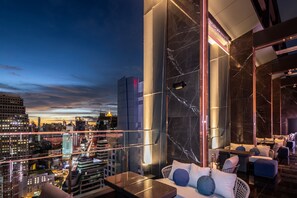 A high-rise hotel room with a city view, modern furnishings, and a marble accent wall.