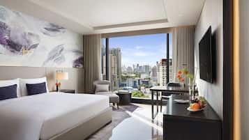 A modern hotel room with a large bed, a desk, a chair, and a city view.