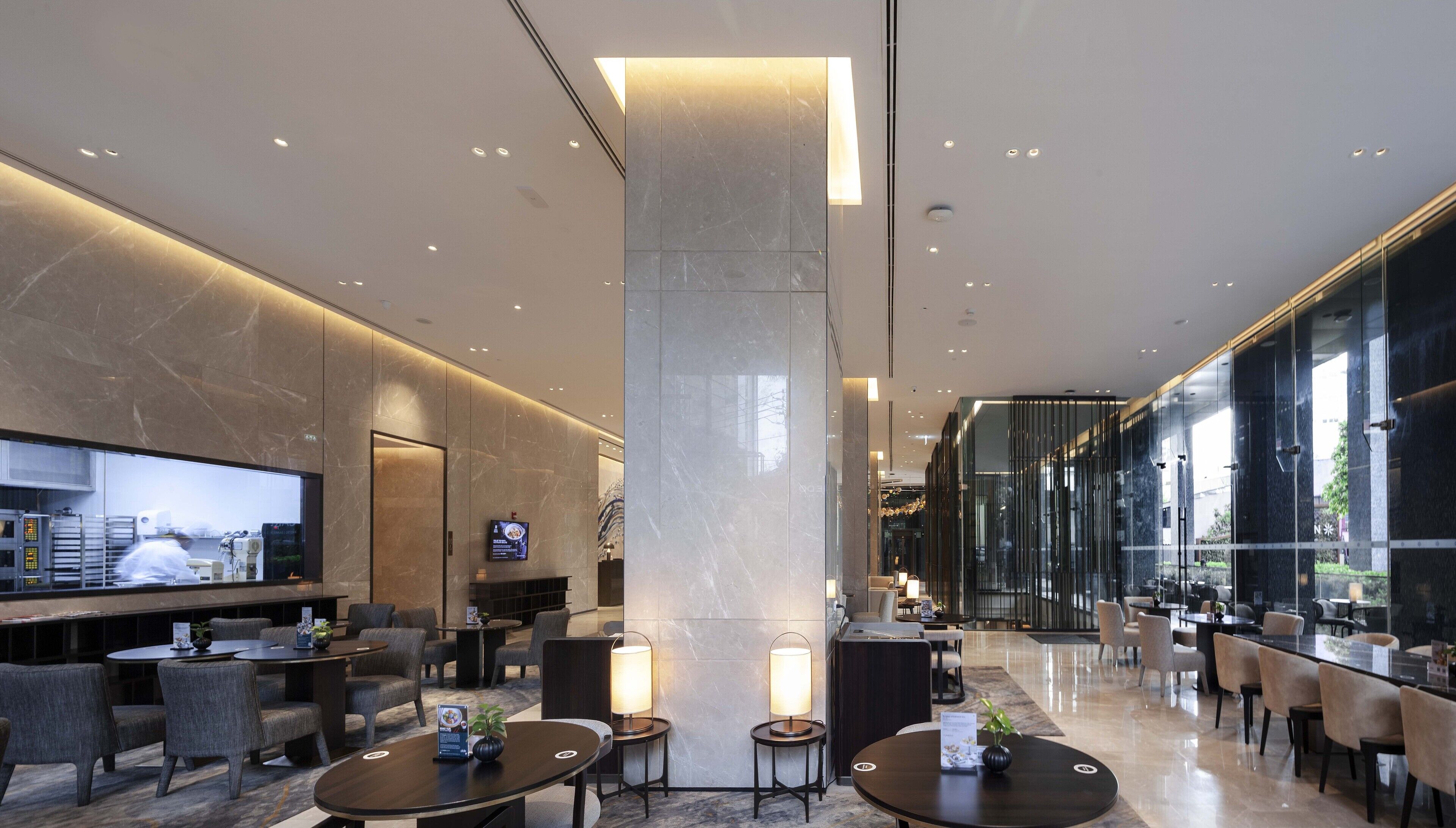 A modern hotel lobby with marble columns, seating areas, and a television screen.