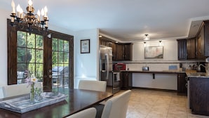 A modern kitchen with dark wood cabinets, stainless steel appliances, and a dining area with a wooden table and white chairs. - Waterfront Cottage - Mystic, Westerly, Stonington Beaches and Casinos Nearby (Stonington)