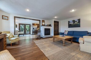 A spacious living room with hardwood flooring, a fireplace, a blue sofa, and a dining table.
