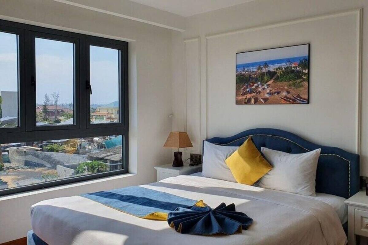 Ein Hotelzimmer mit einem großen Bett, einem Nachttisch, einer Lampe und einem Bild von einer Strandlandschaft.