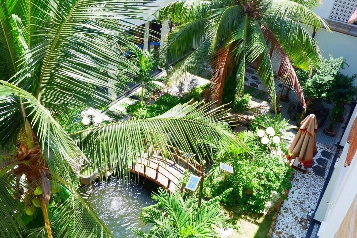 Ein Innenhof mit Palmen, einem kleinen Teich und einer Brücke.