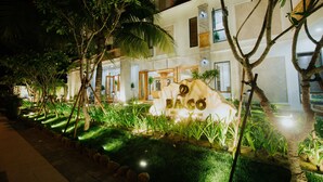 A well-lit building with a sign reading "BACO" in the foreground, surrounded by lush greenery and palm trees. - Ba Co Boutique Hotel (Da Nang)