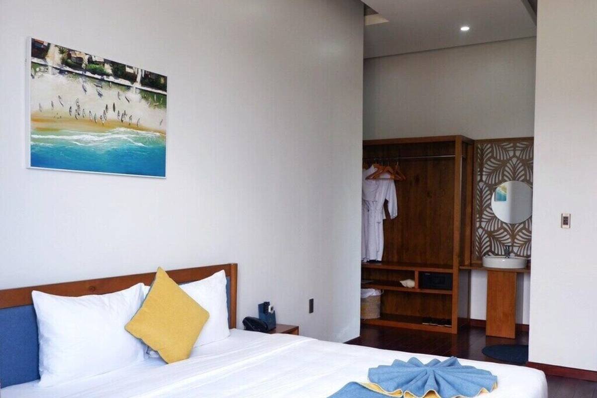 Ein Hotelzimmer mit Bett, einem Strandbild, einem Kleiderschrank und einem Badezimmer mit Spiegel und Waschbecken.