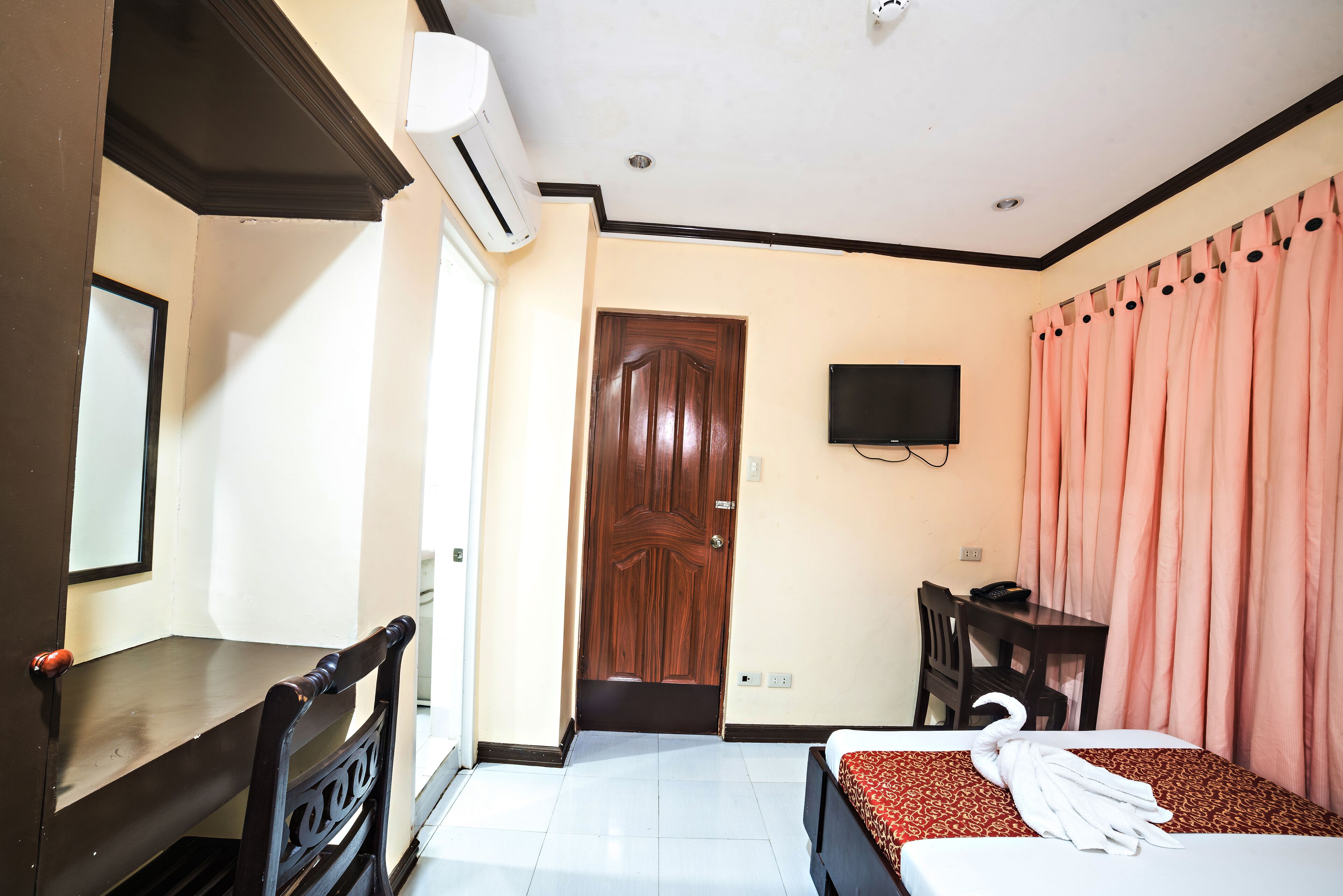 A hotel room with a bed, a desk, a chair, a TV, and a door.