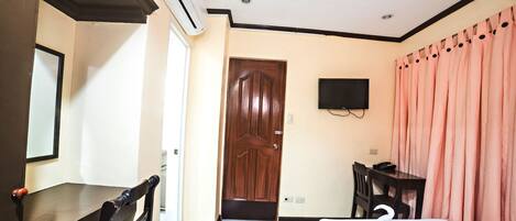 A hotel room with a bed, a desk, a chair, a TV, and a door.