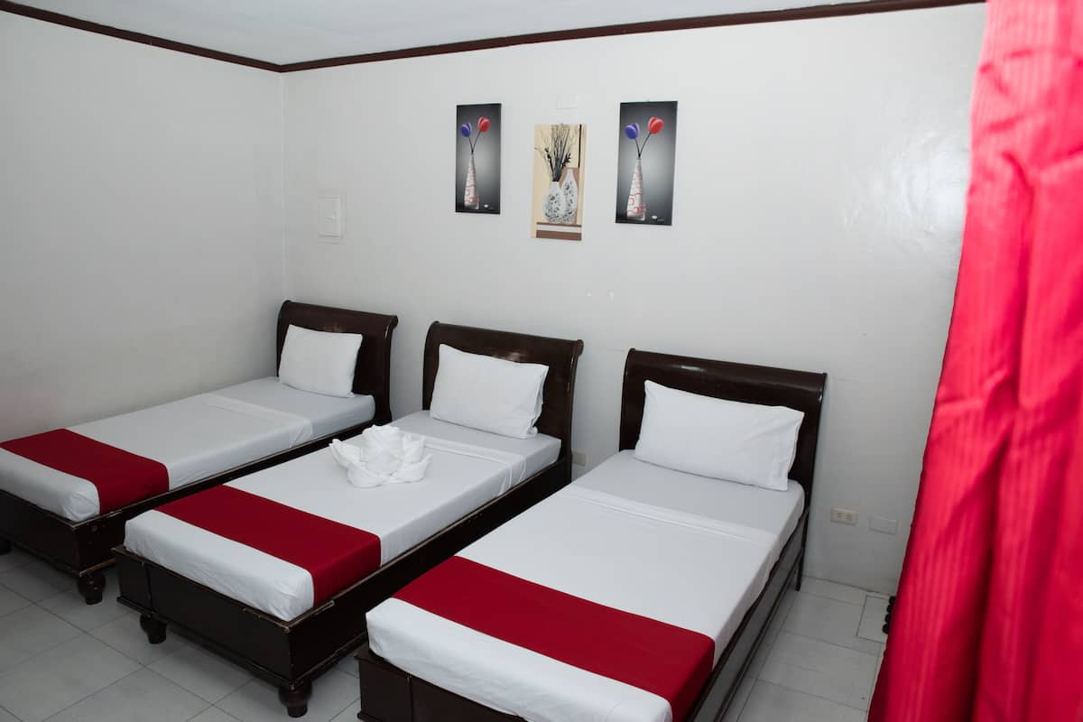 Habitación de hotel con tres camas individuales, cada una con ropa de cama blanca y detalles en rojo. Hay tres cuadros enmarcados en la pared sobre las camas.