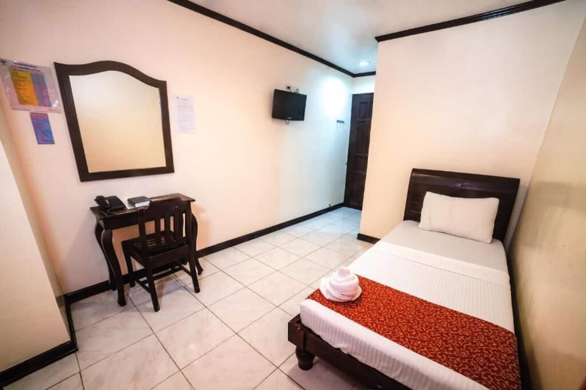 Una habitación de hotel con cama, escritorio, silla, televisor y espejo en la pared.
