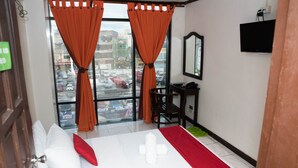 Habitación de hotel con cama, escritorio, silla, televisión y ventana con cortinas.