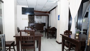 Un comedor con mesas y sillas de madera, una zona de bar con mostrador y copas de vino, y un televisor fijado a la pared.