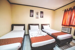 A hotel room with three single beds, each with a red and white bedspread, white pillows, and a white towel on the bed. There is a wall-mounted air conditioning unit to the right and three framed pictures above the beds. - Peach Tree Lodge (Ormoc)