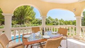 An outdoor dining area with a glass table, wicker chairs, and a view of a swimming pool and greenery. - Gorgeous home in Trullent (Trullent)