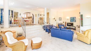 A spacious living area with a blue sofa set, wicker chairs, and a yellow sofa. A staircase leads to a dining area with a table and chairs. - Gorgeous home in Trullent (Trullent)