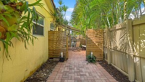 A narrow brick pathway leading to a wooden gate, surrounded by lush greenery and a yellow building. -  Beach getaway 1 bdrm, private patio! STEPS TO BEACH! Summer Sale! (Boca Raton)