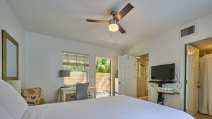 Ein Schlafzimmer mit einem großen Bett, einem Schreibtisch mit Stuhl, einem Fernseher und einem Deckenventilator.
