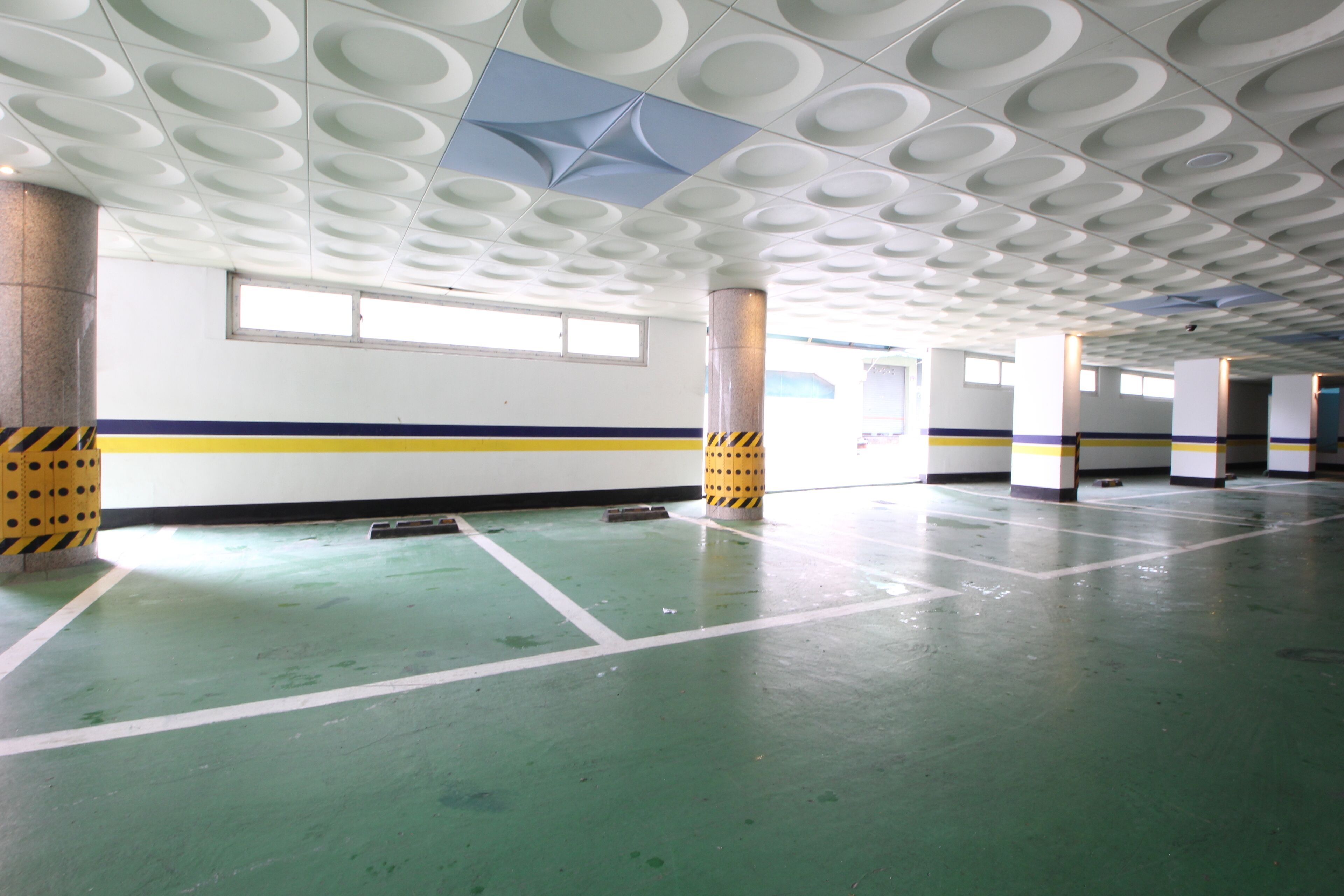 Un garaje para estacionar con pisos verdes, paredes blancas y columnas a rayas negras y amarillas.
