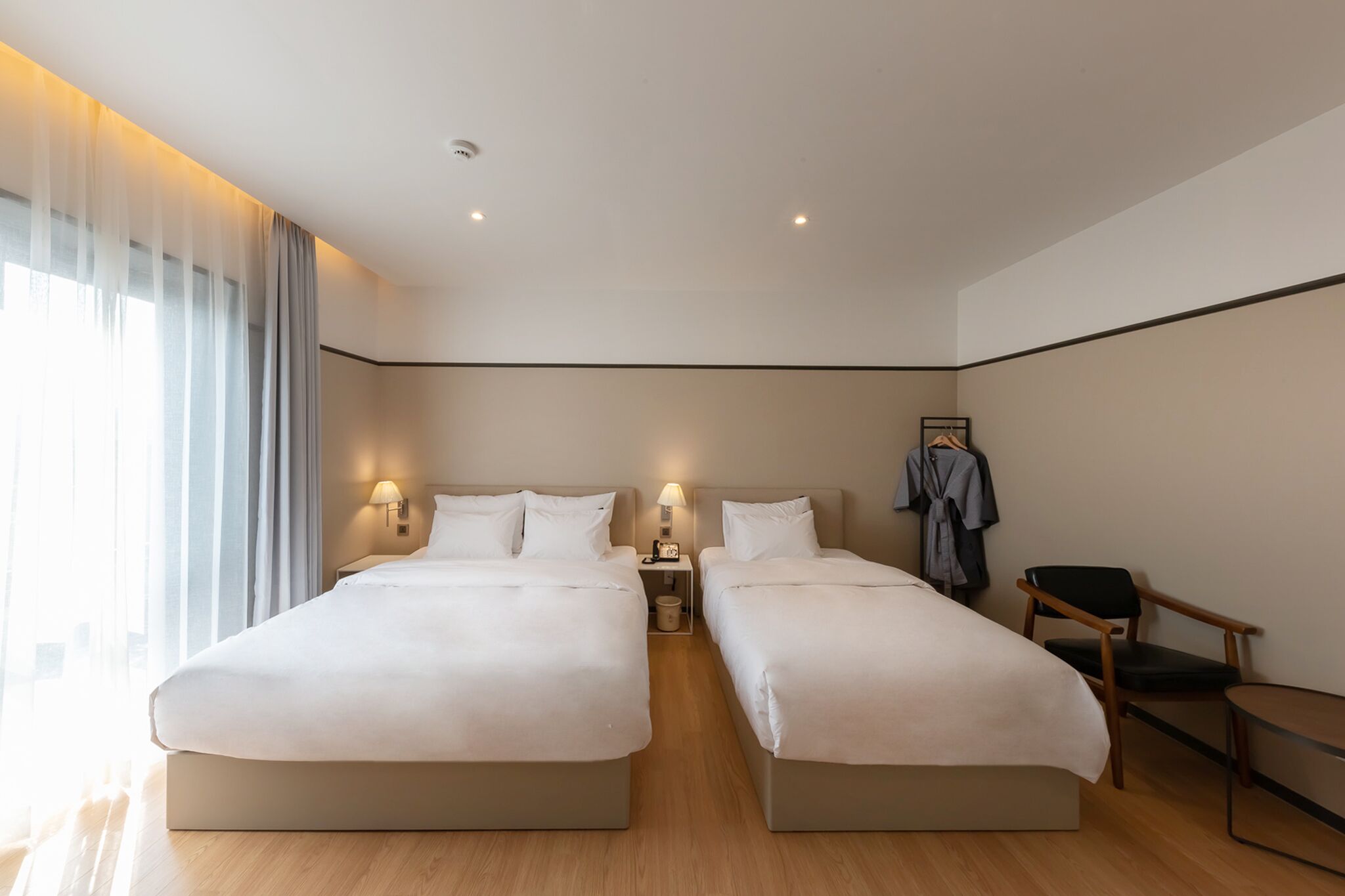 A hotel room with two beds, a desk, a chair, and a wardrobe.
