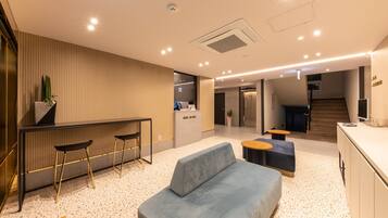 A modern hotel lobby with a reception desk, seating area, and a staircase leading to other floors.